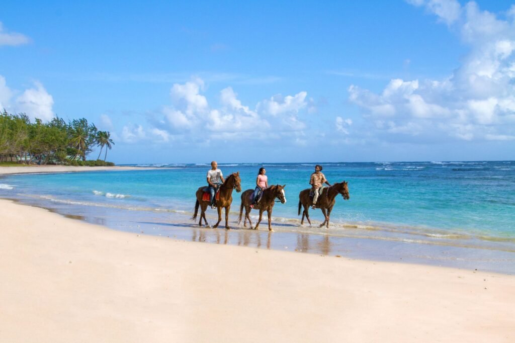Turistas montando a caballo en la orilla de la playa de Barbados, una de las experiencias más relajantes y únicas del Caribe.