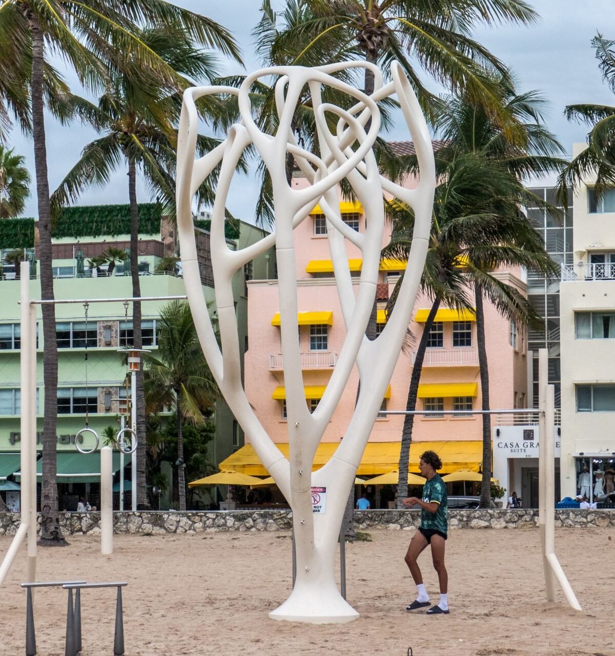Escultura contemporánea en la playa de Miami Beach con edificios Art Déco de Ocean Drive al fondo."