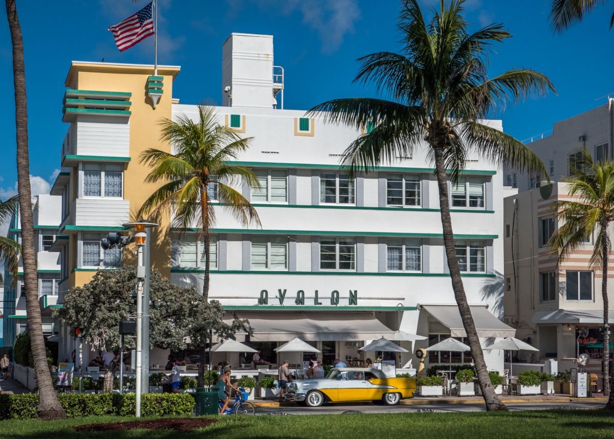 Hotel Avalon en Ocean Drive, Miami Beach, con arquitectura Art Déco y un auto clásico amarillo estacionado al frente.