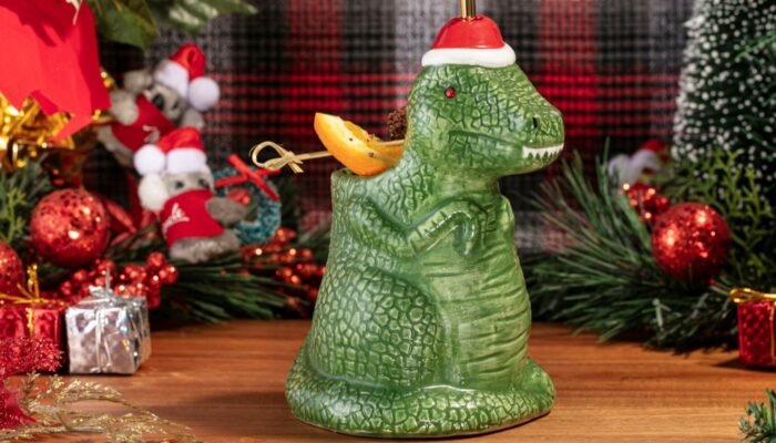 Cóctel navideño en taza de dinosaurio con gorro de Santa, rodeado de decoraciones festivas en Panamá.