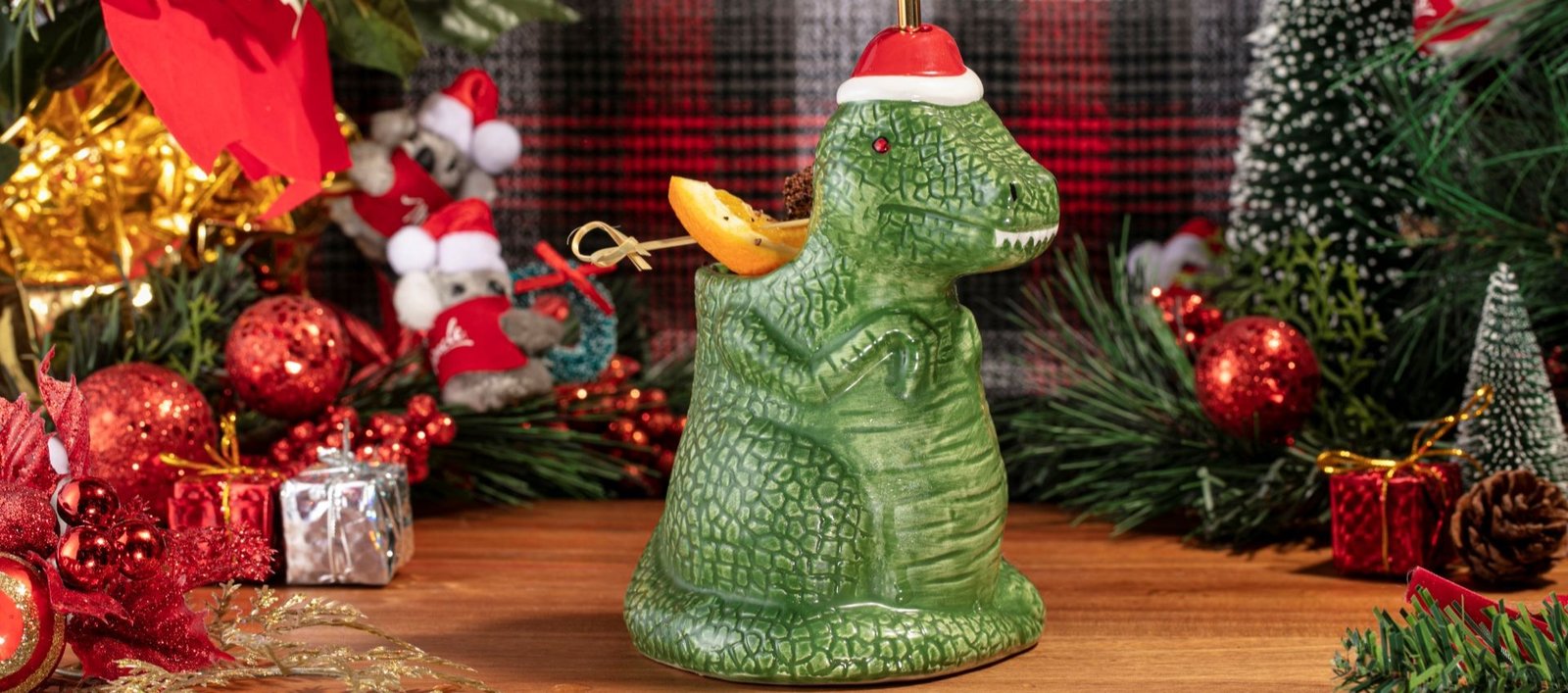 Cóctel navideño en taza de dinosaurio con gorro de Santa, rodeado de decoraciones festivas en Panamá.
