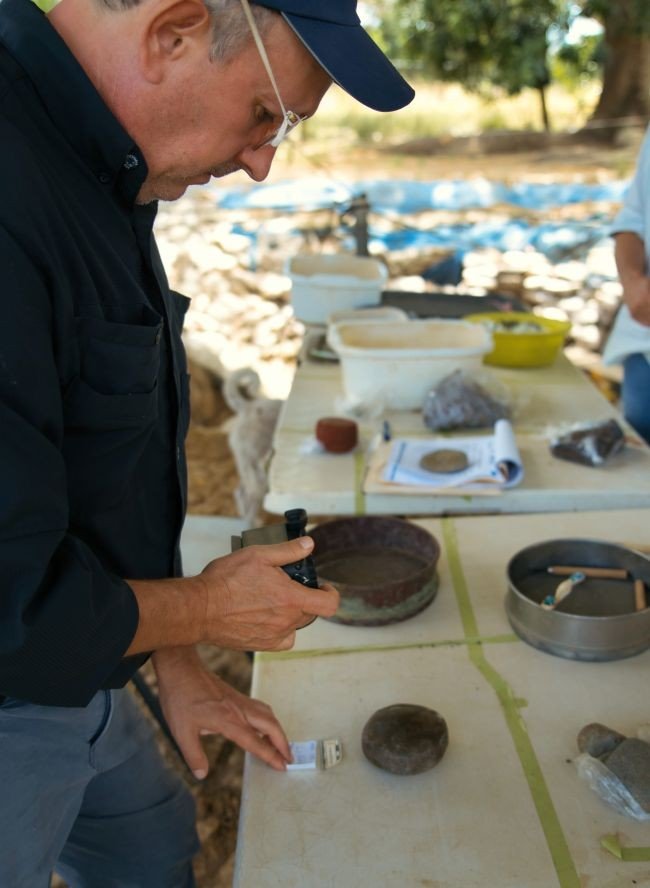 Carlos Mayo Torné, investigador del Proyecto Arqueológico El Caño fotografiando una herramienta (martillo-bruñidor) de ágata, a pie de la excavación. El Caño, 0026.